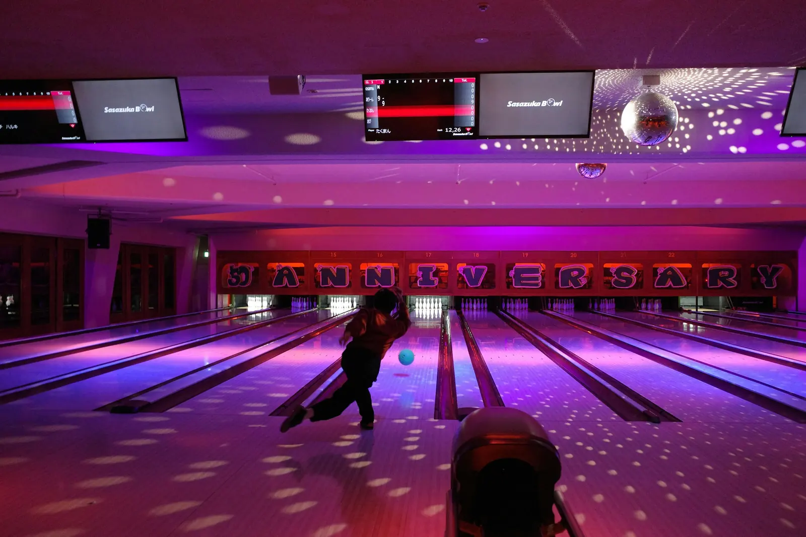 A bowler mid-throw in a neon-lit bowling alley