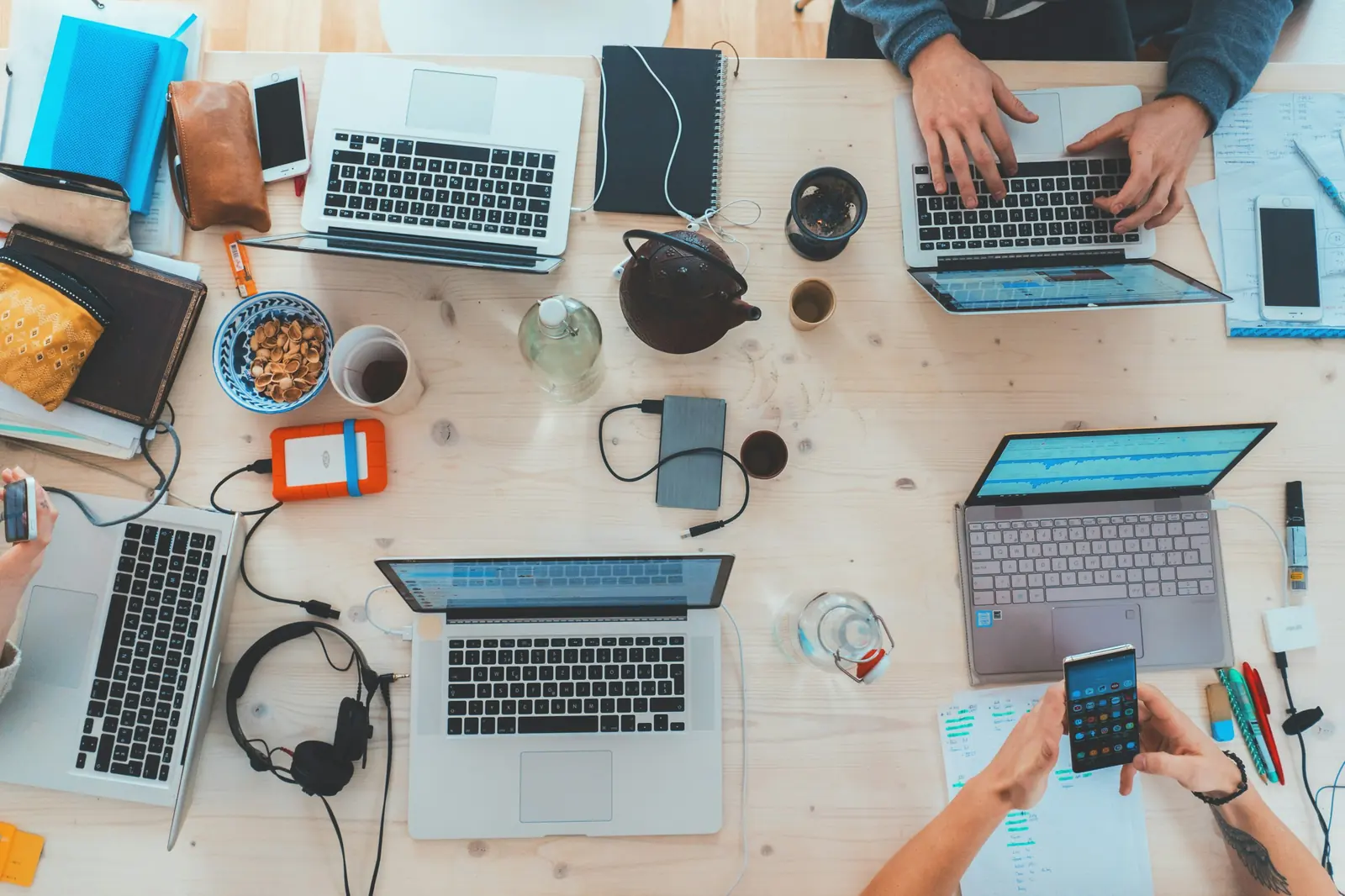 A shared desk from above, with laptops, notebooks and phones